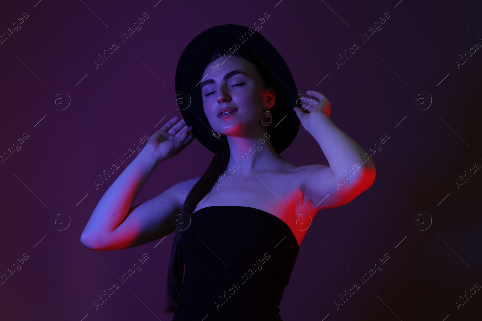 Photo of Portrait of beautiful young woman in hat on color background with neon lights