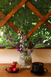 Bouquet of beautiful wildflowers, aromatic coffee and fresh strawberries on wooden table