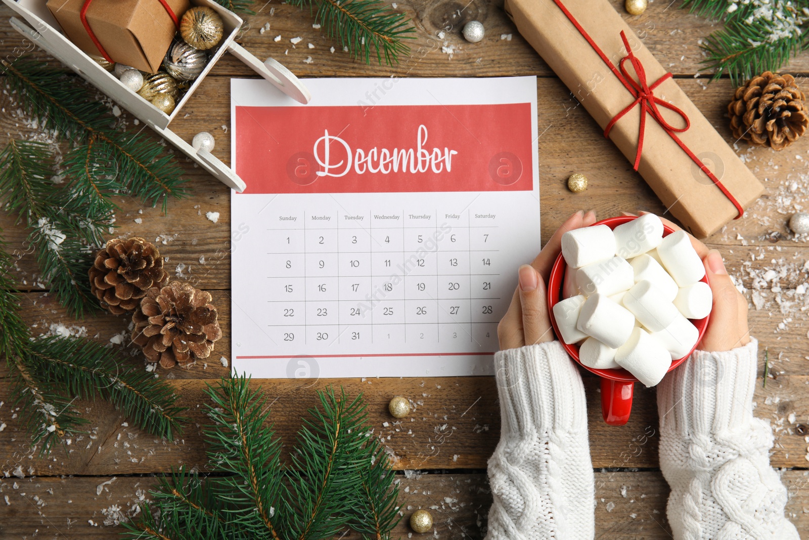 Photo of Woman holding hot drink near paper calendar at wooden table, top view