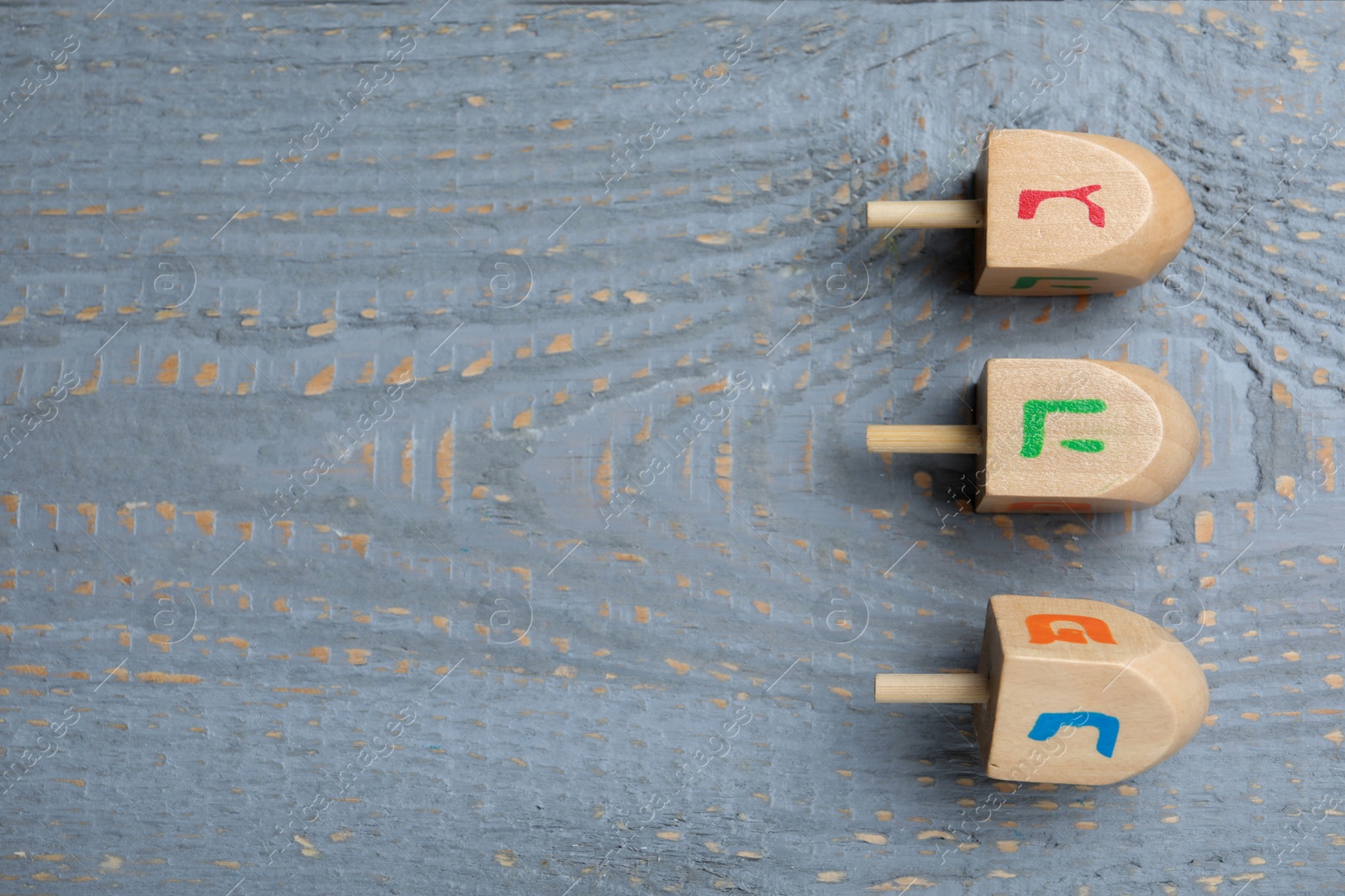 Photo of Hanukkah traditional dreidels on grey wooden table, flat lay. Space for text