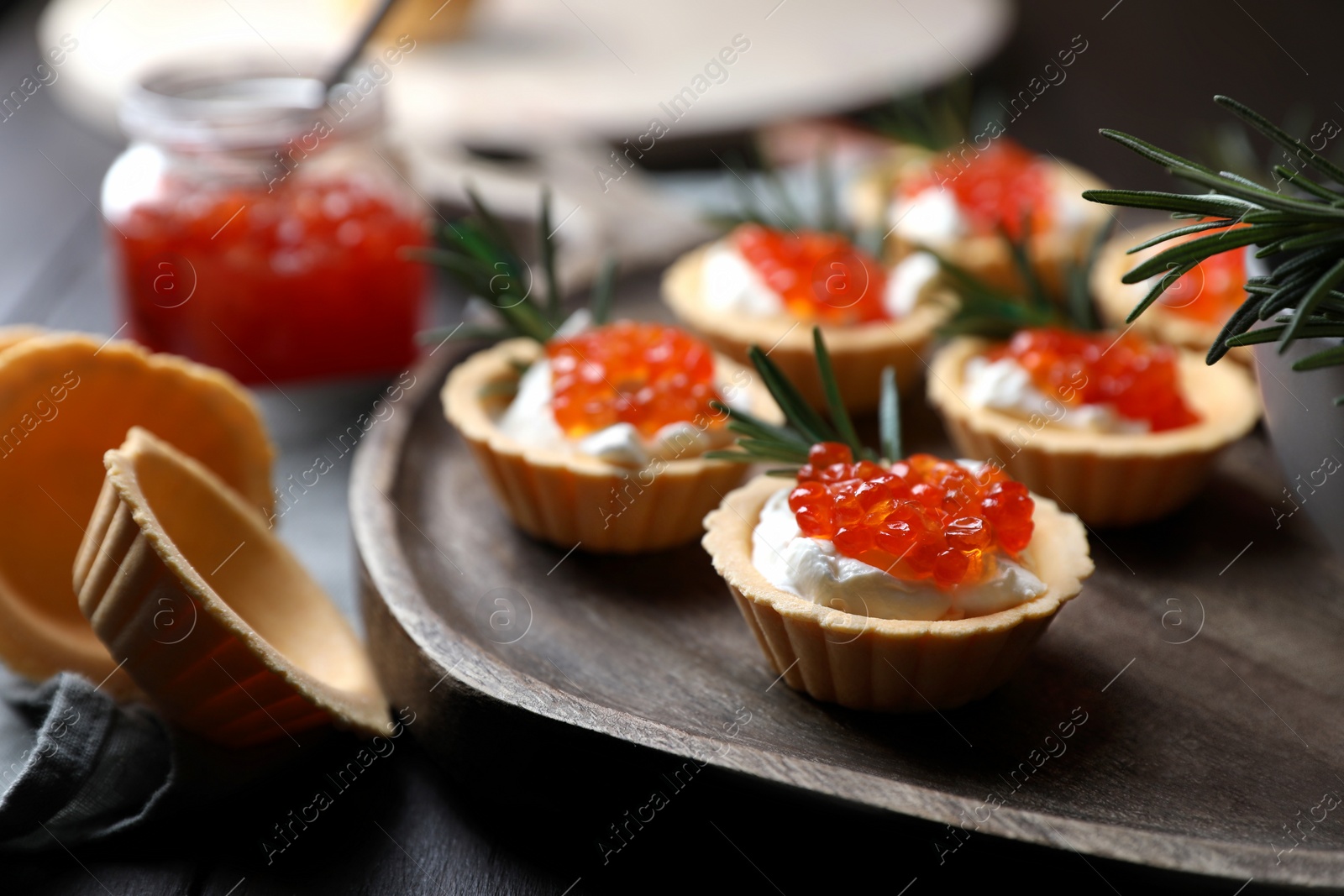 Photo of Delicious tartlets with red caviar and cream cheese served on wooden table, closeup