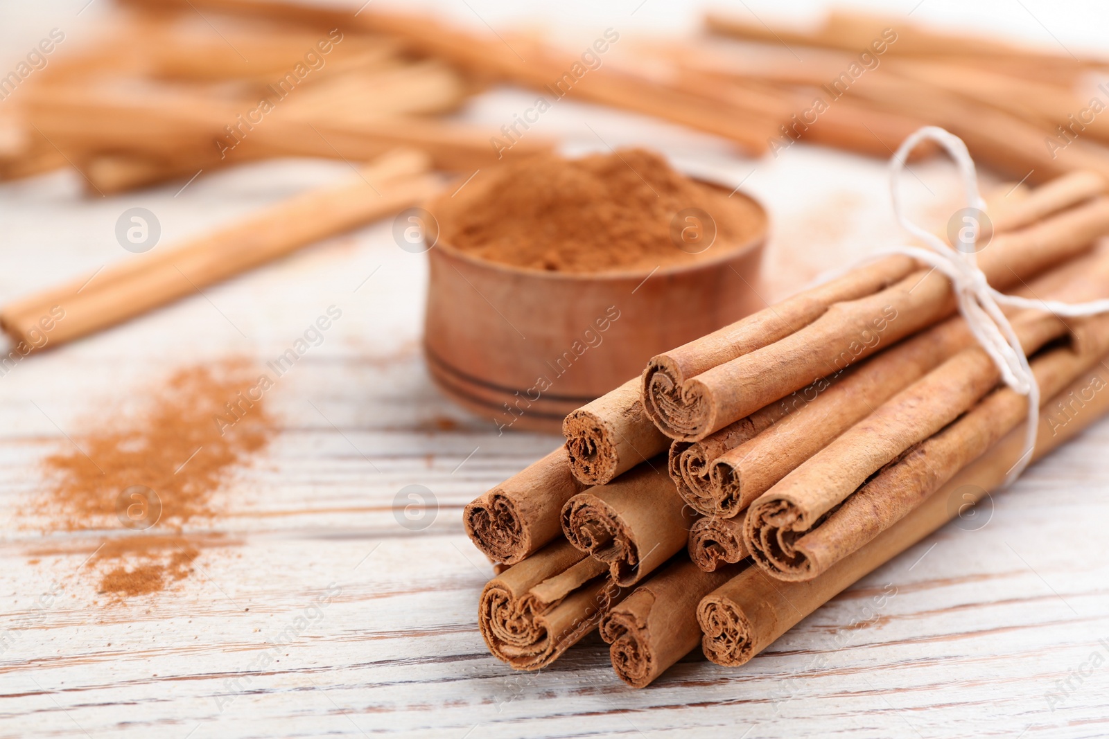 Photo of Aromatic cinnamon sticks on white wooden table, closeup. Space for text