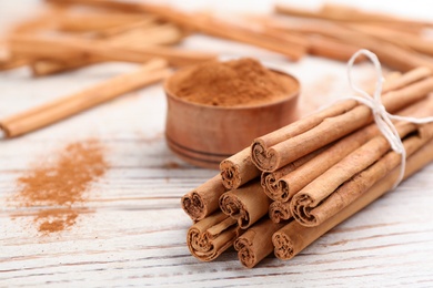 Photo of Aromatic cinnamon sticks on white wooden table, closeup. Space for text