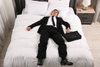 Photo of Businessman with briefcase sleeping on bed indoors