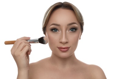 Beautiful young woman applying face powder with brush on white background