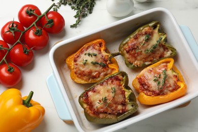 Photo of Tasty stuffed peppers in dish and ingredients on white table, flat lay