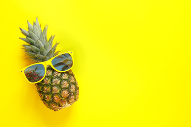 Pineapple and sunglasses with reflection of palm trees on yellow background, top view. Space for text
