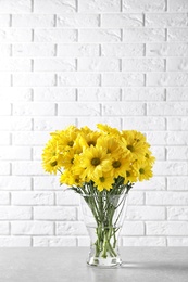 Vase with beautiful chamomile flowers on table against brick wall