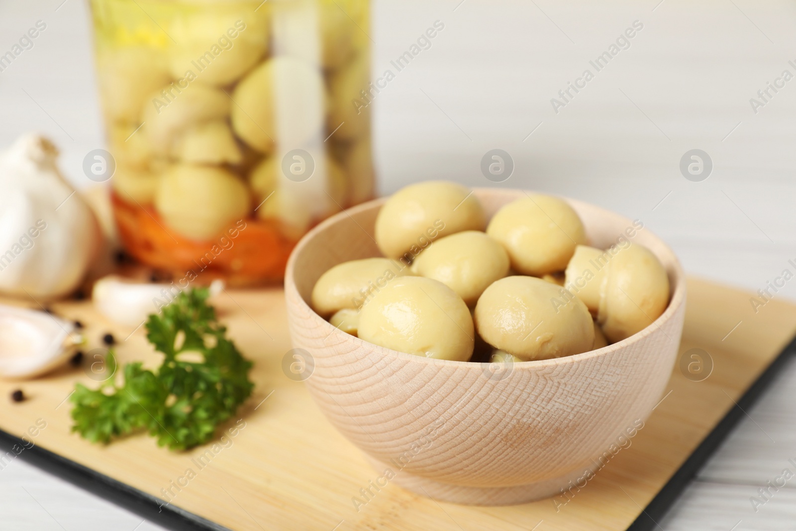 Photo of Bowl with delicious pickled mushrooms on white wooden table