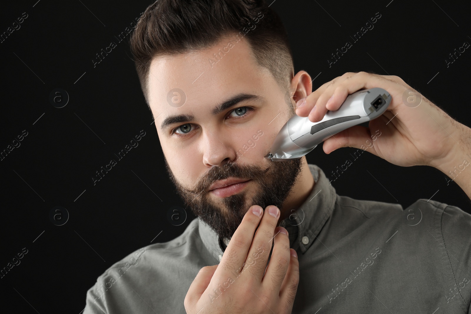 Photo of Handsome young man trimming beard on black background