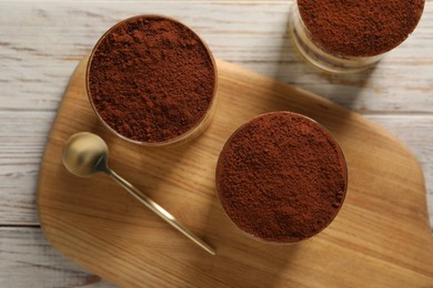 Photo of Delicious tiramisu in glasses and spoon on light wooden table, top view