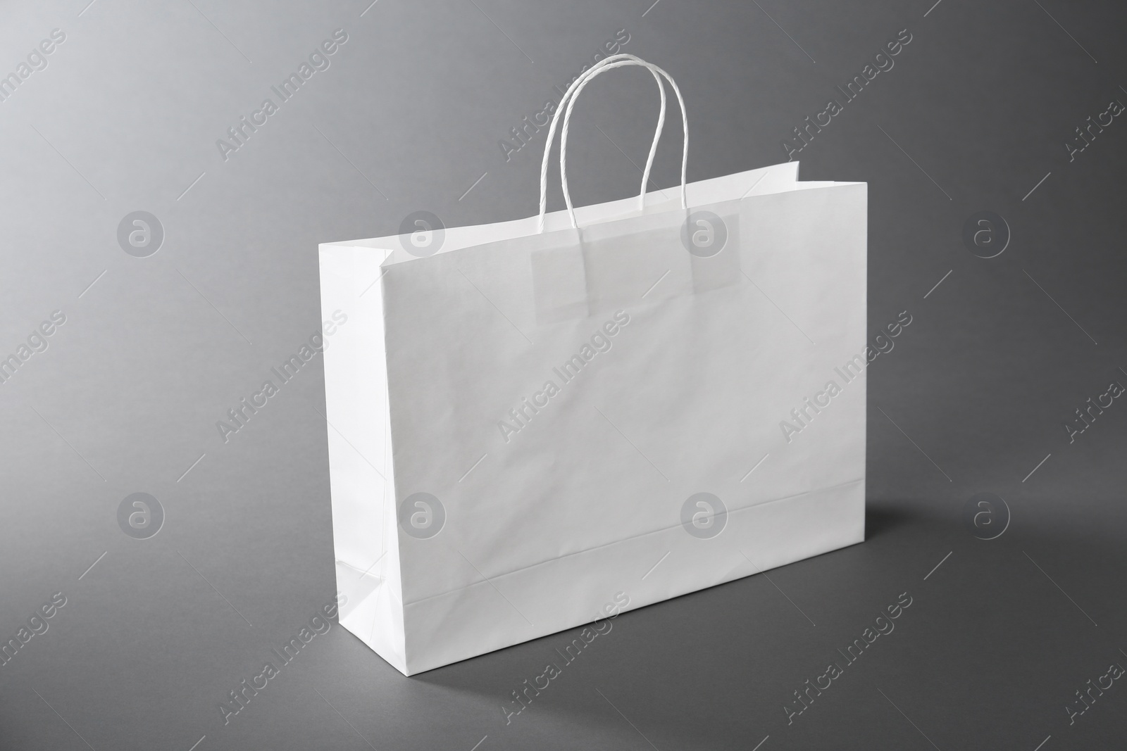 Photo of One white paper bag on grey background. Mockup for design