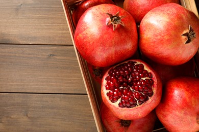 Photo of Ripe pomegranates in crate on wooden table, top view. Space for text