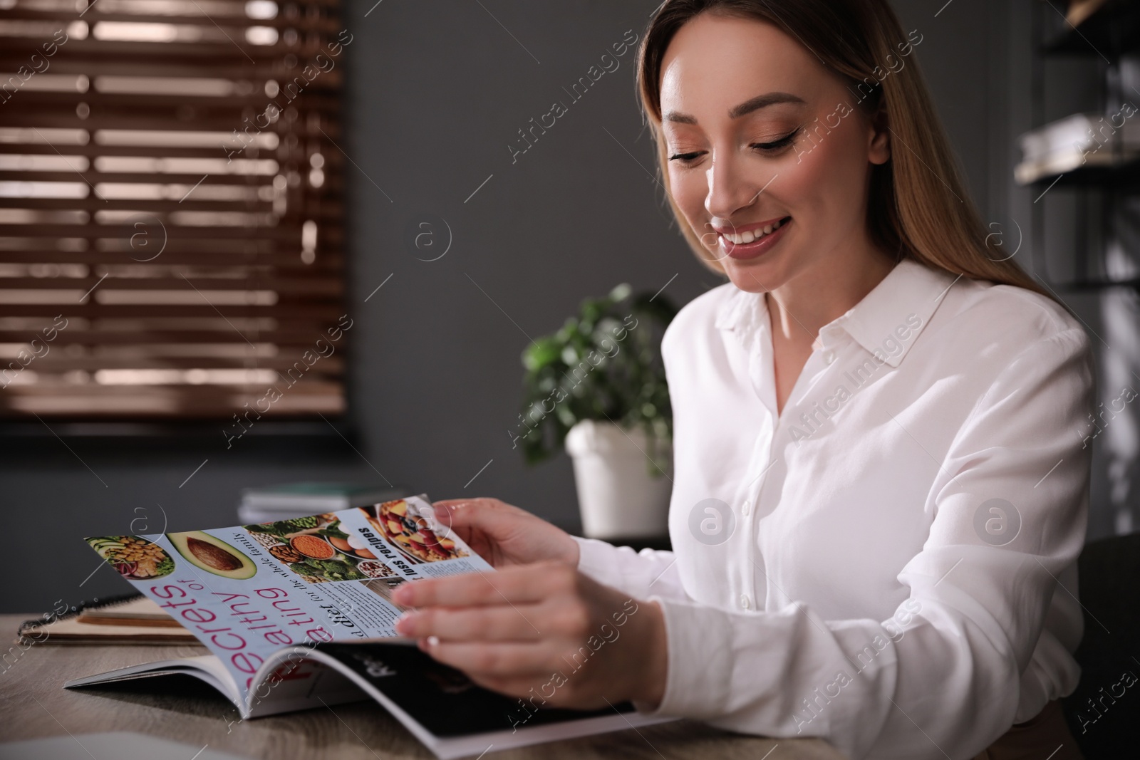 Photo of Happy woman reading magazine at workplace in office