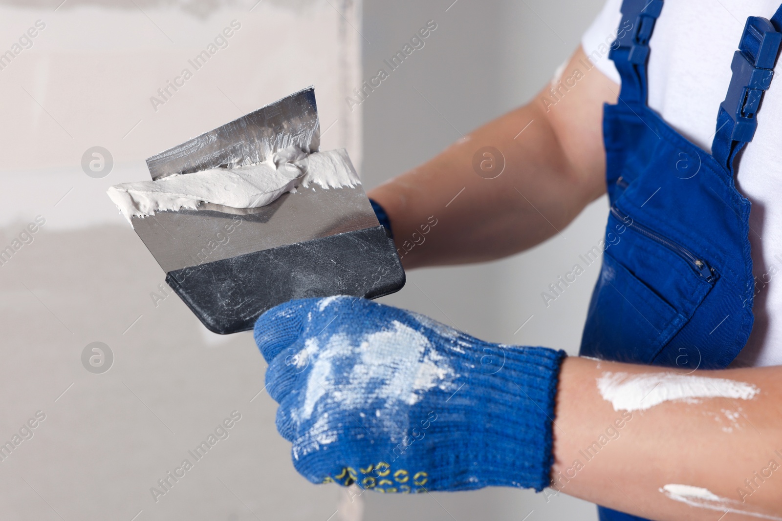 Photo of Worker with putty knives and plaster near wall indoors, closeup. Home renovation