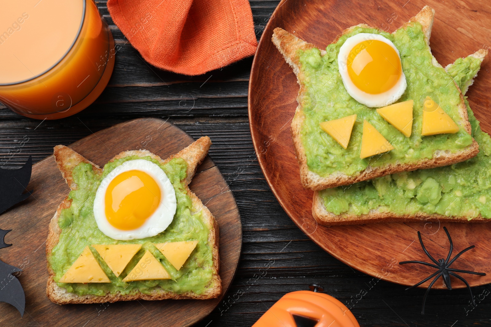 Photo of Halloween themed breakfast served on black wooden table, flat lay. Tasty sandwiches with fried eggs