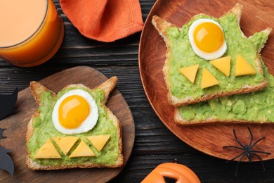 Photo of Halloween themed breakfast served on black wooden table, flat lay. Tasty sandwiches with fried eggs
