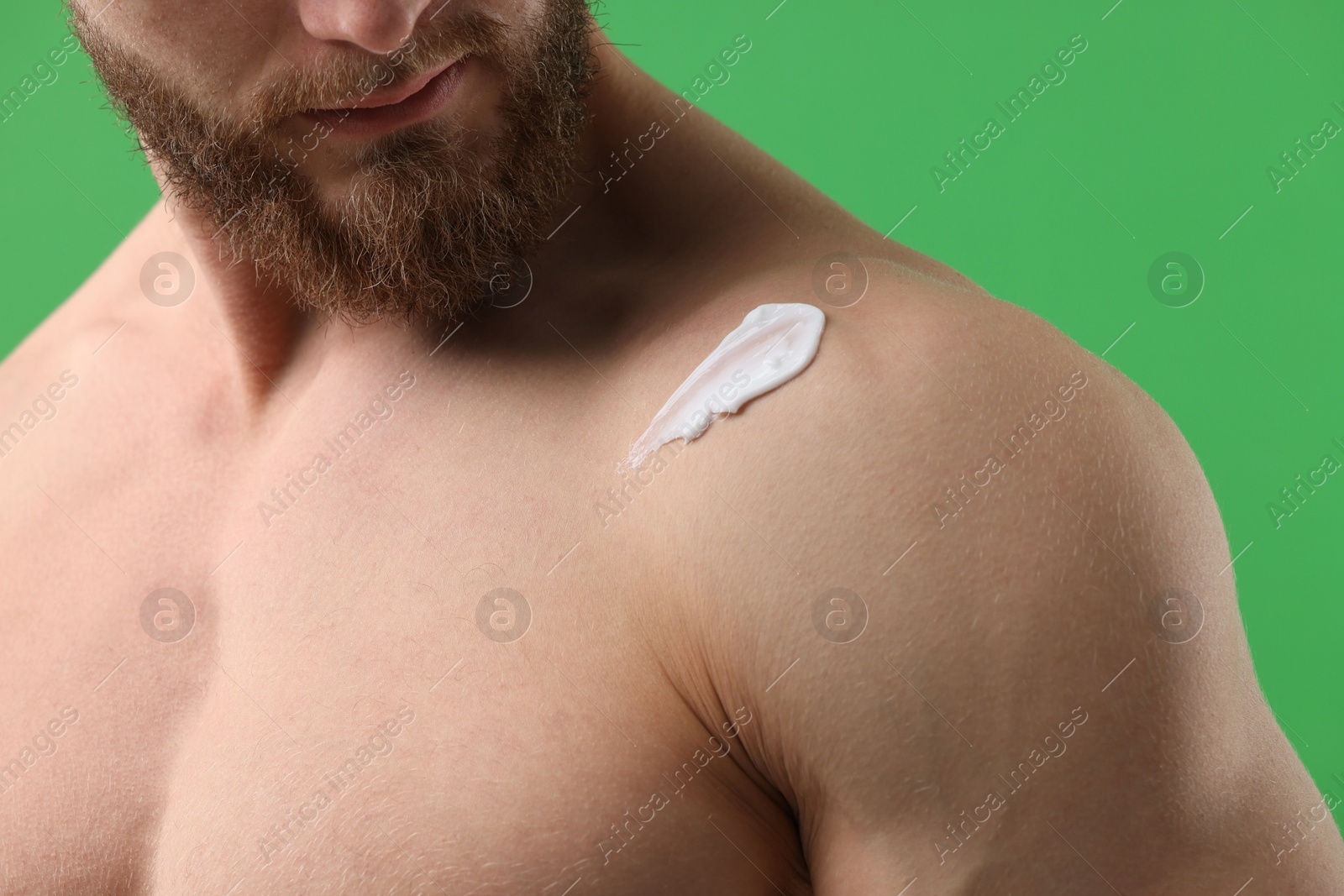 Photo of Man with moisturizing cream on his shoulder against green background, closeup