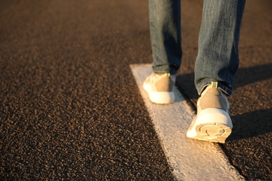 Photo of Man walking along white line on road, closeup with space for text. Way concept