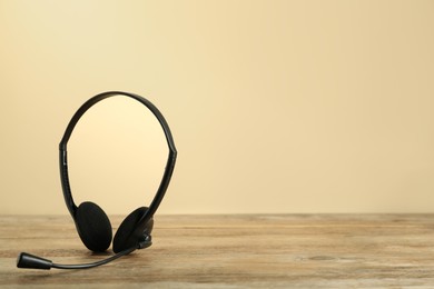 Photo of Headset on wooden table against beige background, space for text