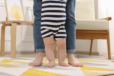 Mother supporting her baby son while he learning to walk on carpet at home, closeup