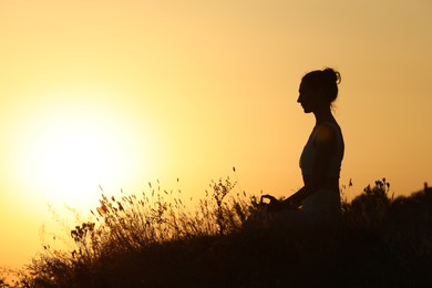 Photo of Silhouette of woman meditating outdoors at sunset. Space for text
