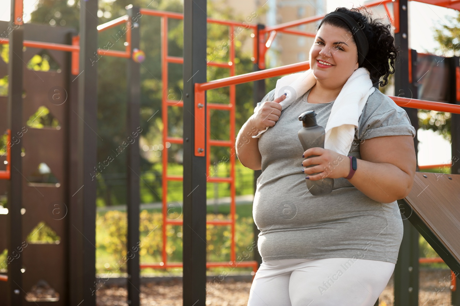 Photo of Beautiful overweight woman with towel and bottle on sports ground