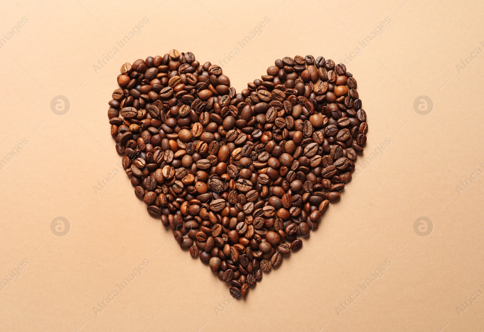 Photo of Heart shaped pile of coffee beans on light orange background, top view
