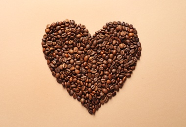 Heart shaped pile of coffee beans on light orange background, top view