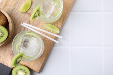 Photo of Refreshing drink, cut kiwi and lime on white tiled table, flat lay. Space for text
