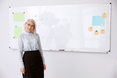 Photo of Mature teacher near whiteboard in modern classroom. Space for text