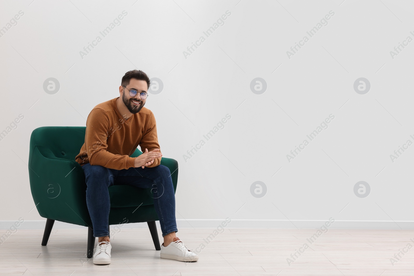 Photo of Handsome man sitting in armchair near white wall indoors, space for text