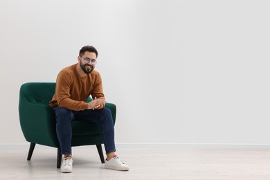 Photo of Handsome man sitting in armchair near white wall indoors, space for text