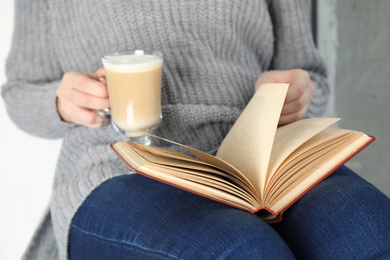 Photo of Woman with cup of coffee reading book at home, closeup