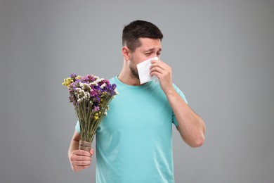 Allergy symptom. Man with bunch of flowers sneezing on light grey background
