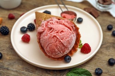Photo of Delicious pink ice cream in wafer cone with berries on wooden table, closeup