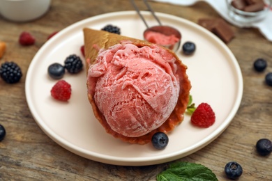 Delicious pink ice cream in wafer cone with berries on wooden table, closeup