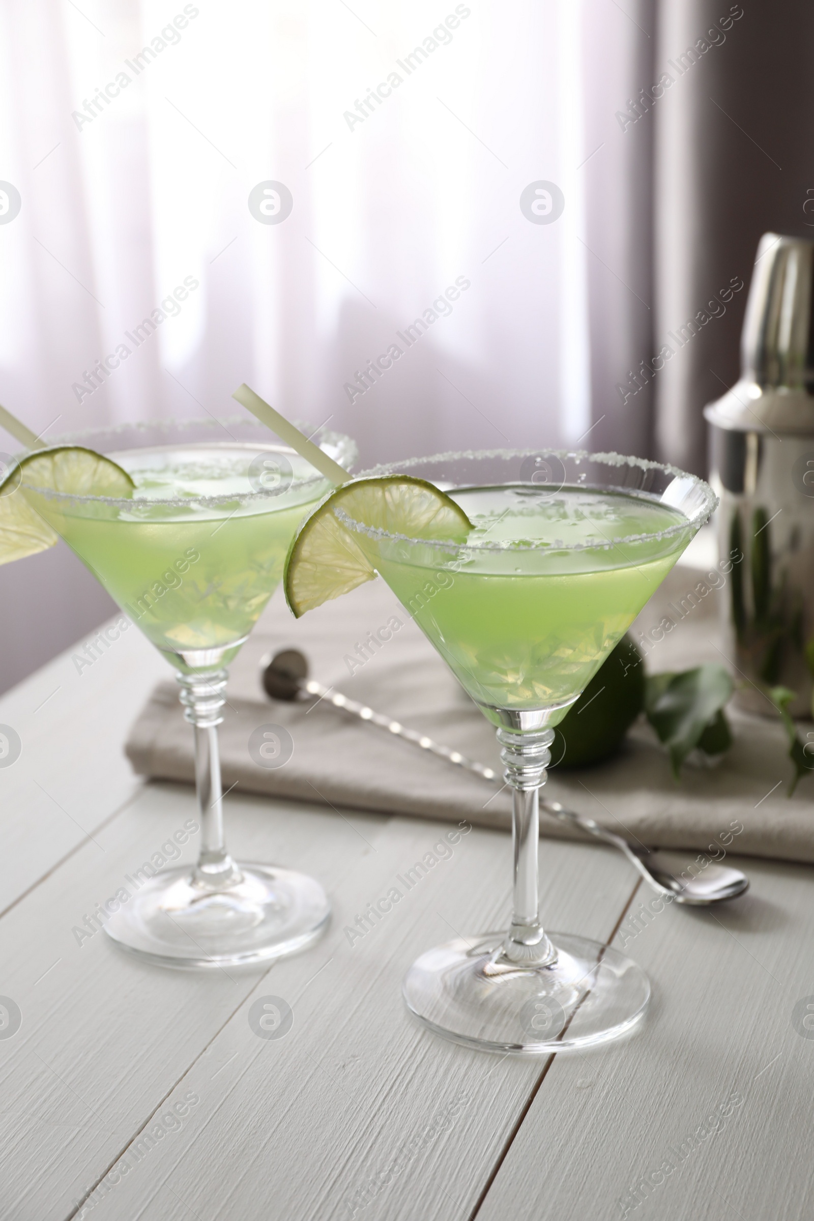 Photo of Delicious Margarita cocktail in glasses, lime and bar spoon on white wooden table