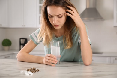 Photo of Woman holding glass of medicine for hangover in kitchen