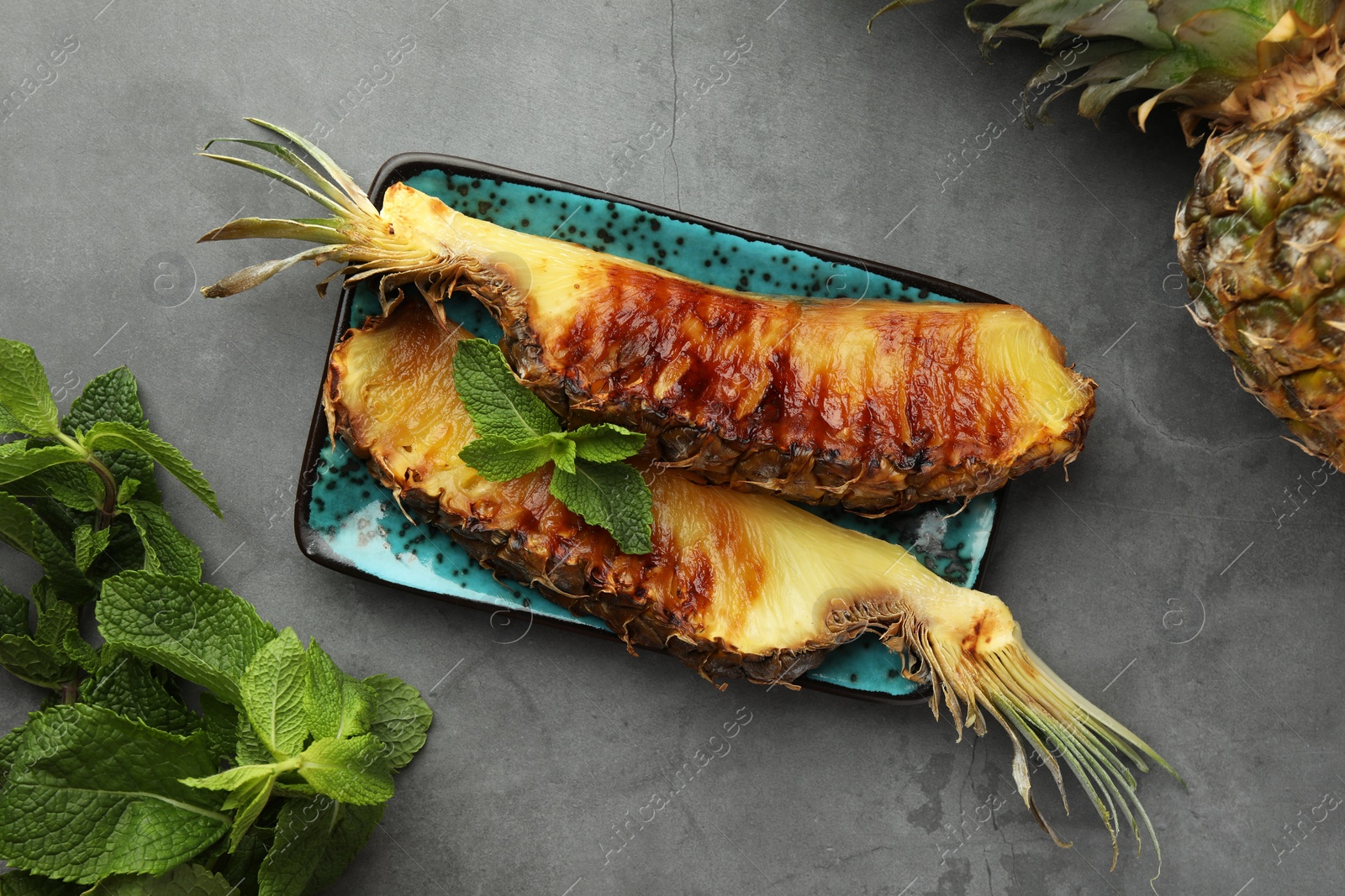 Photo of Tasty grilled pineapple pieces and mint leaves on grey textured table, flat lay