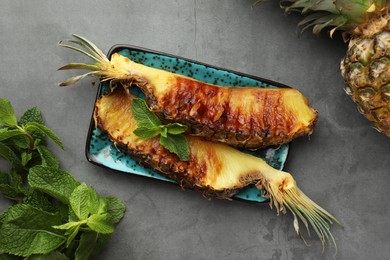 Tasty grilled pineapple pieces and mint leaves on grey textured table, flat lay