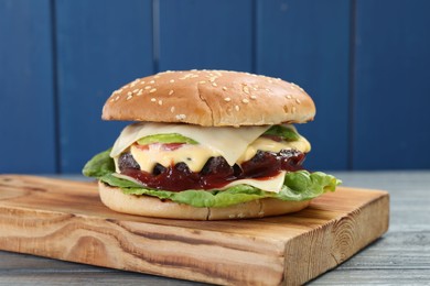 Photo of Tasty homemade cheeseburger with lettuce on grey wooden table, closeup