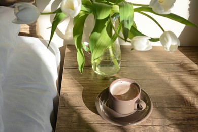 Photo of Beautiful white tulip bouquet and cup of coffee on nightstand in bedroom