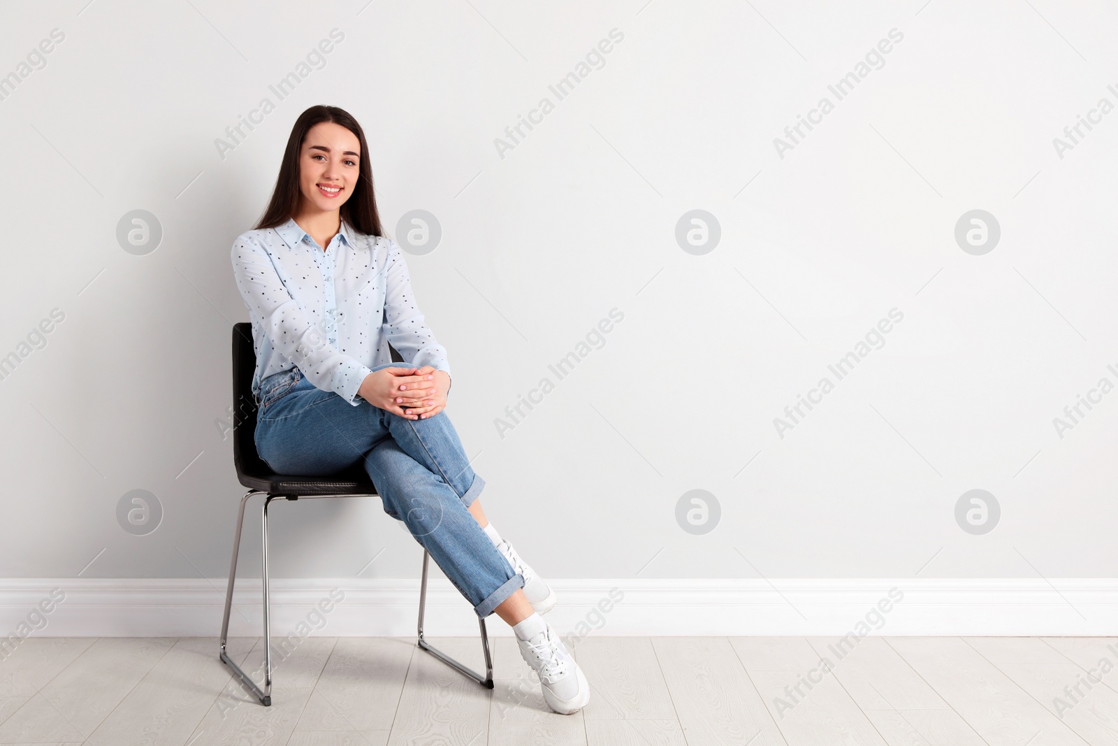 Photo of Young woman sitting on chair near white wall in office, space for text