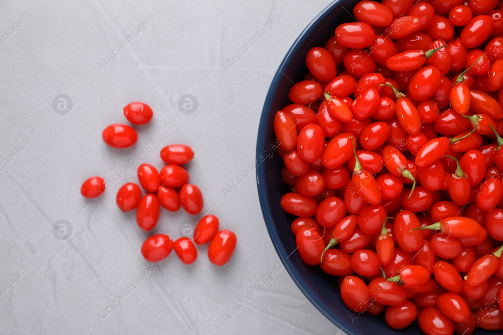 Photo of Bowl with fresh goji berries on grey background, flat lay