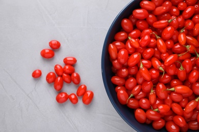 Photo of Bowl with fresh goji berries on grey background, flat lay