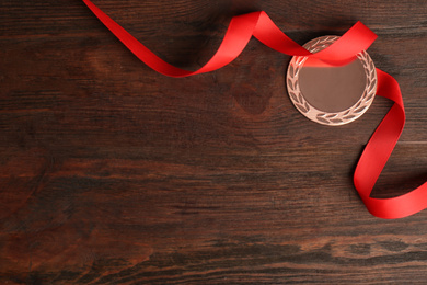 Photo of Bronze medal with red ribbon on wooden background, flat lay. Space for design