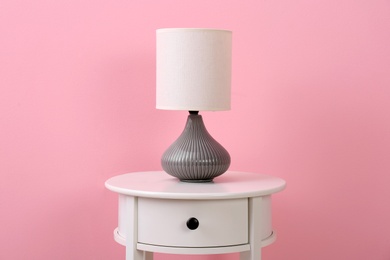 Photo of Stylish lamp on table against color background