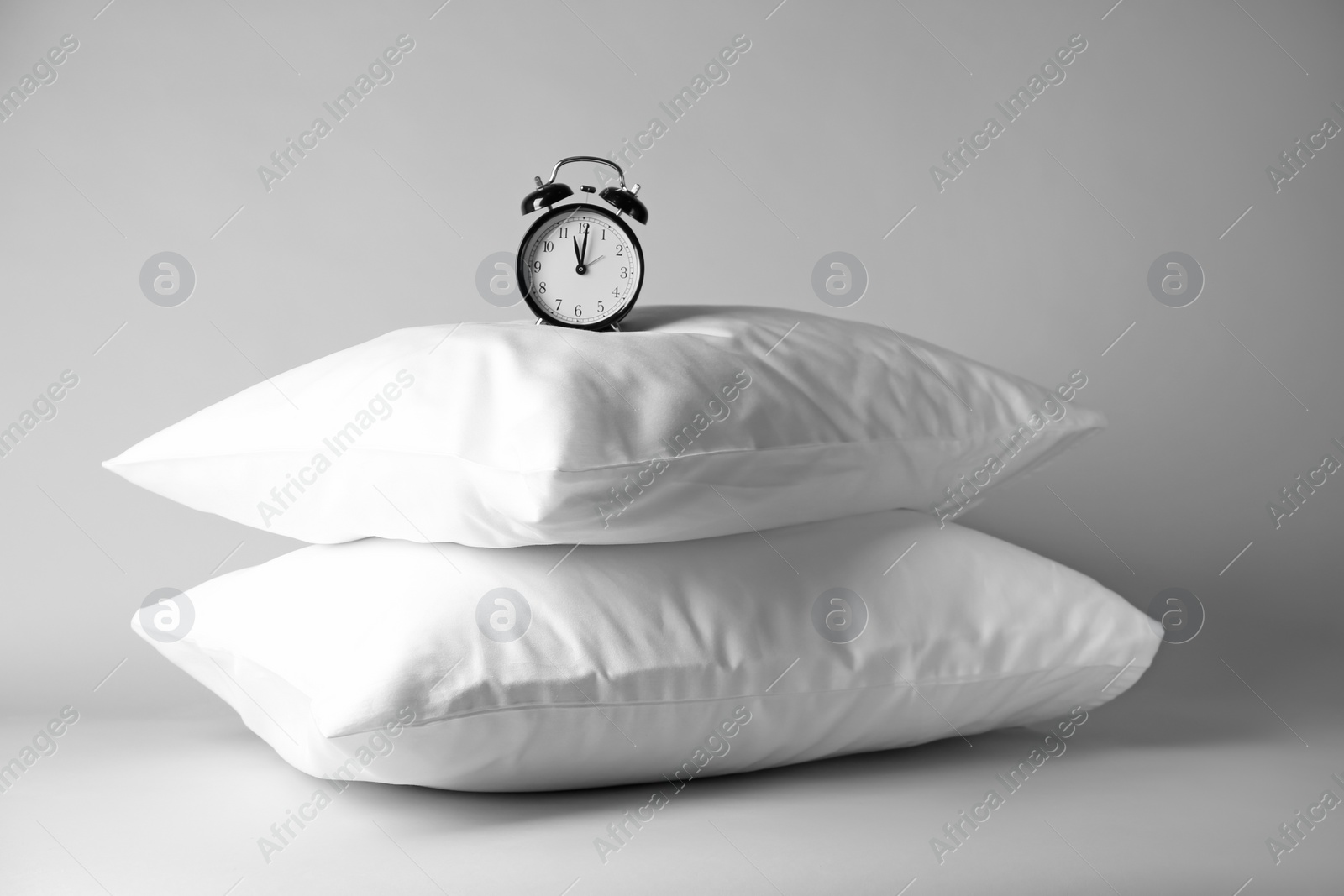 Photo of Soft pillows and alarm clock on light background