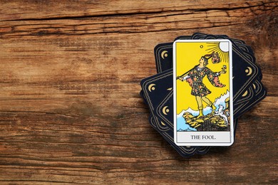 Photo of The Fool and other tarot cards on wooden table, flat lay. Space for text